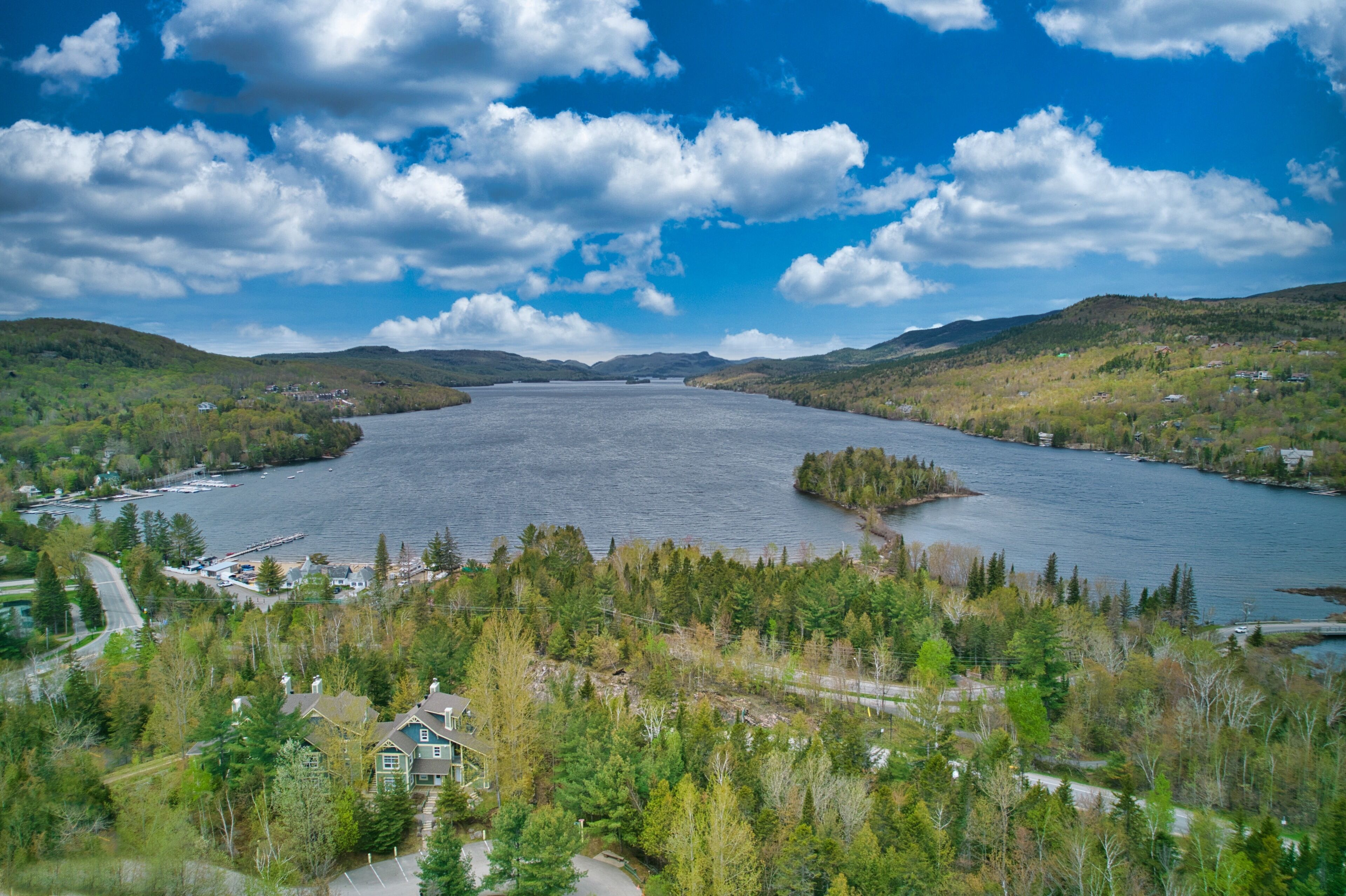 A large body of water surrounded by hills and trees, with a small dock and houses nearby.