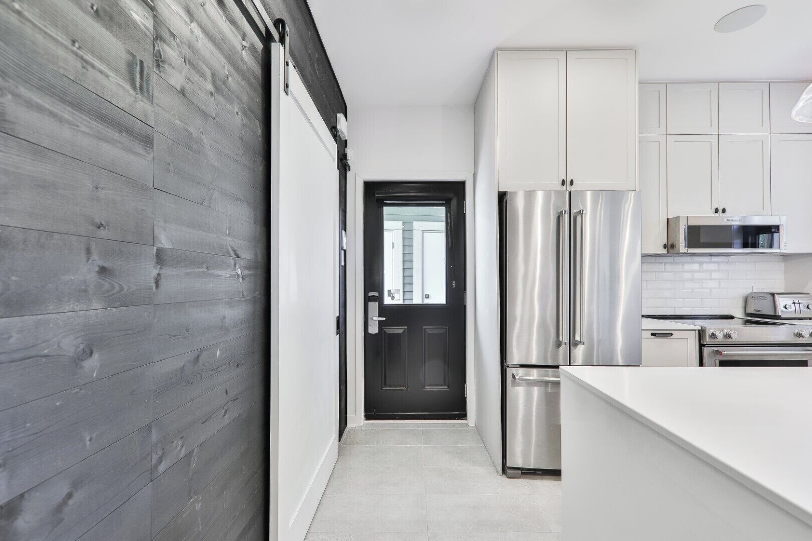 A modern kitchen with stainless steel appliances, white cabinetry, and a dark wooden accent wall.