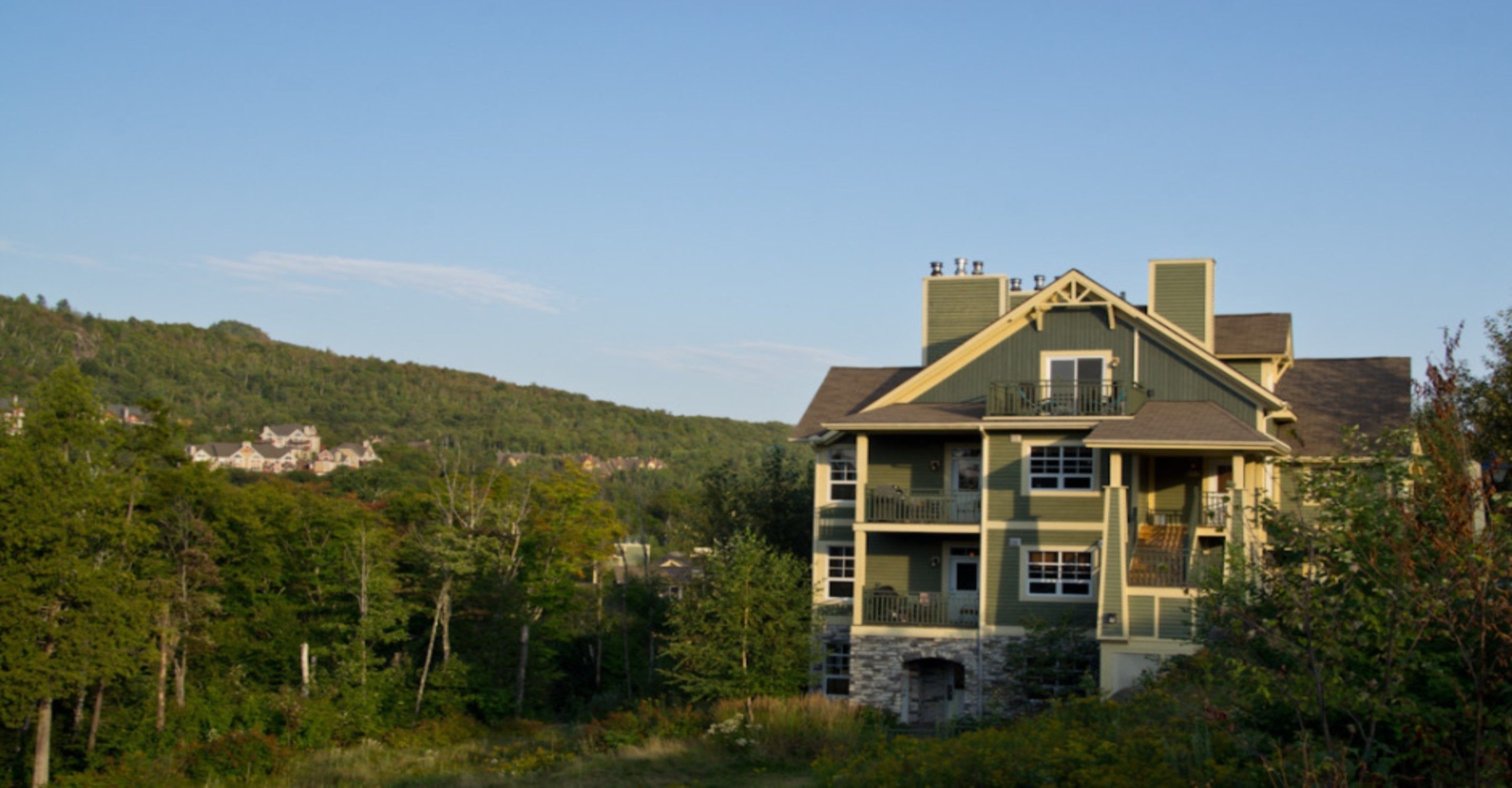 A two-story building with a stone foundation, multiple balconies, and a view of a forested hillside.
