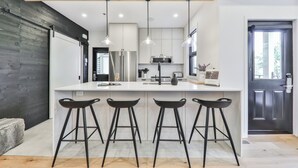 Una cucina moderna con isola centrale, sgabelli da bar, elettrodomestici in acciaio inossidabile e illuminazione a sospensione.