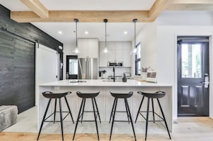 Una cocina moderna con una isla central, taburetes de bar, electrodomésticos de acero inoxidable e iluminación colgante.