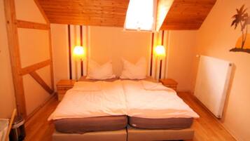 Ein Schlafzimmer mit Holzboden, einem Einzelbett mit weißer und brauner Bettwäsche, zwei Nachttischlampen und einem kleinen Fenster.