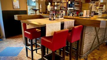 Uma área de bar com balcão de madeira, banquetas vermelhas e piso ladrilhado.