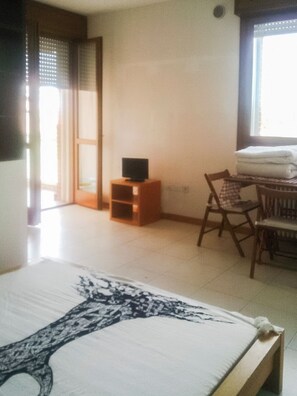 A hotel room with a bed, a television on a stand, a chair, and a table with a folded tablecloth.
