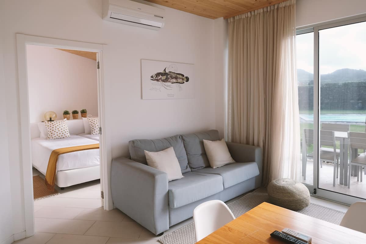 Een moderne woonkamer met een grijze bank, een houten eettafel en een grote schuifdeur die uitkomt op een terras.