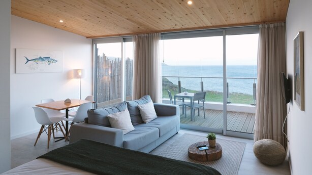 Un dormitorio moderno con un amplio ventanal corredera que da a un balcón con vistas al mar.