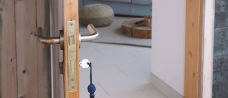 Una puerta de madera con un ojo de cerradura y un cerrojo, que da a un cuarto con un sofá gris, una mesa redonda de centro y un fleco azul colgando de la puerta.