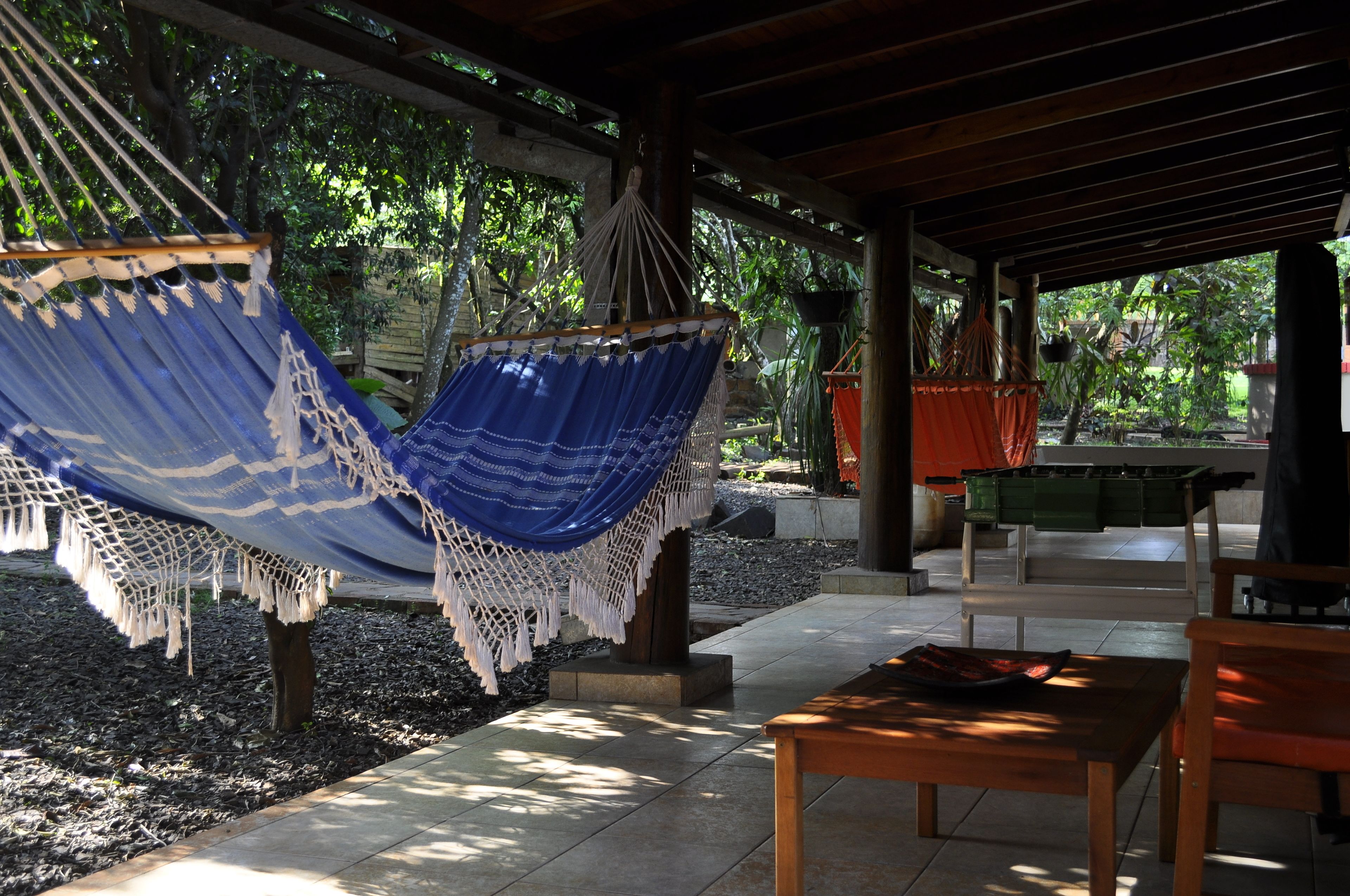 A covered outdoor seating area with a hammock, a wooden table, and a bench.