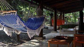 A covered outdoor seating area with a hammock, a wooden table, and a bench.