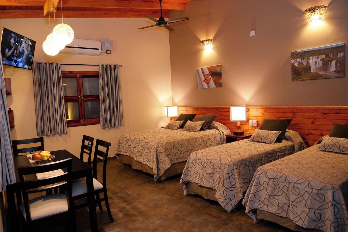 Une chambre d’hôtel avec deux lits, une table à manger avec des chaises, un ventilateur de plafond et un climatiseur fixé au mur.