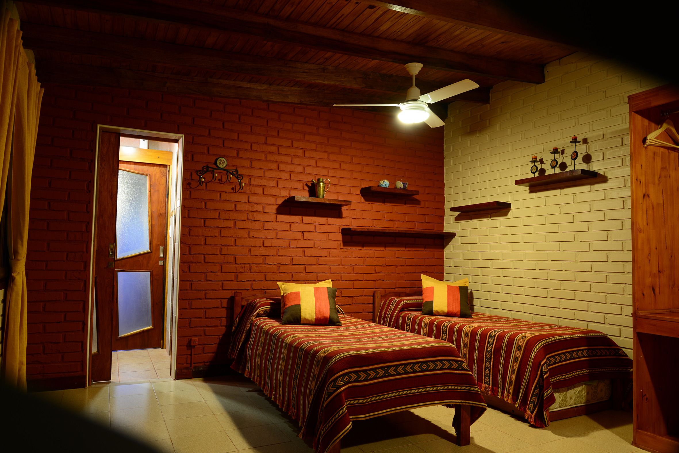 A room with two beds, a ceiling fan, and brick walls.