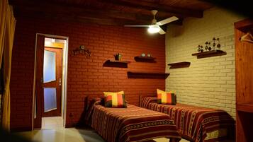 A room with two beds, a ceiling fan, and brick walls.