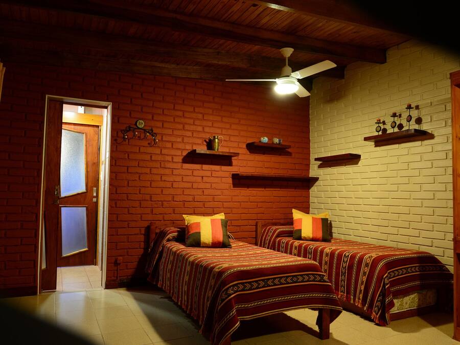 A room with two beds, a ceiling fan, and brick walls.
