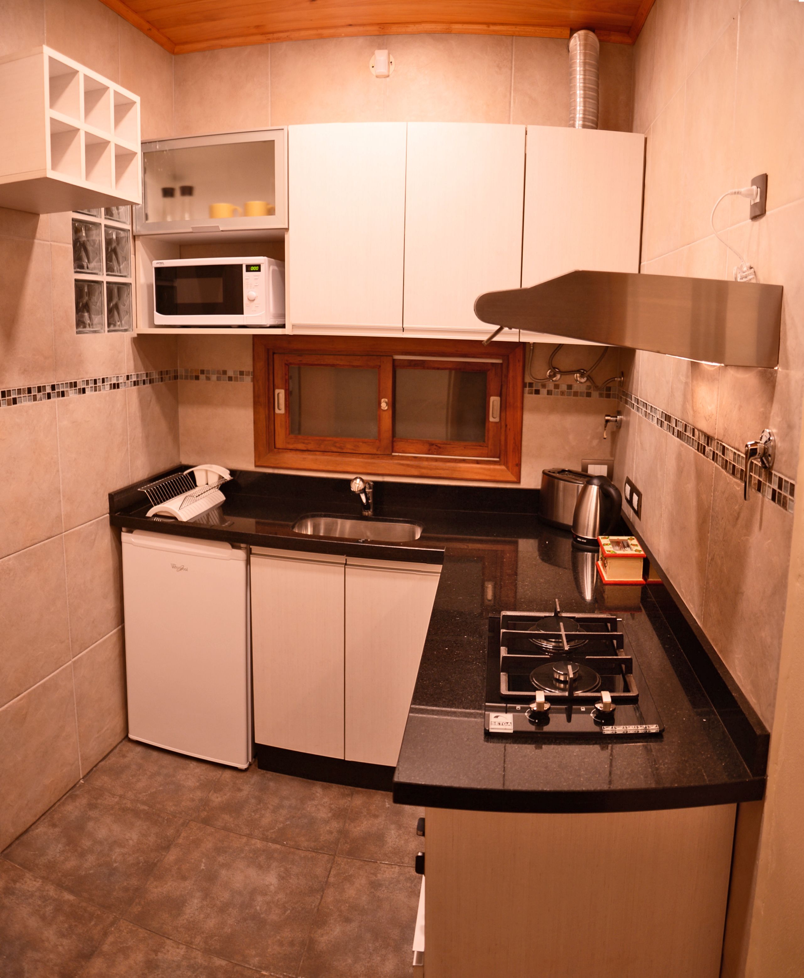 Una cocina compacta con microondas, estufa, lavamanos y armarios de madera.