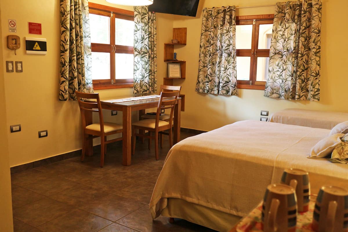 Une chambre d’hôtel comprenant un lit, un bureau avec des chaises, une fenêtre avec des rideaux et un téléviseur fixé au mur.