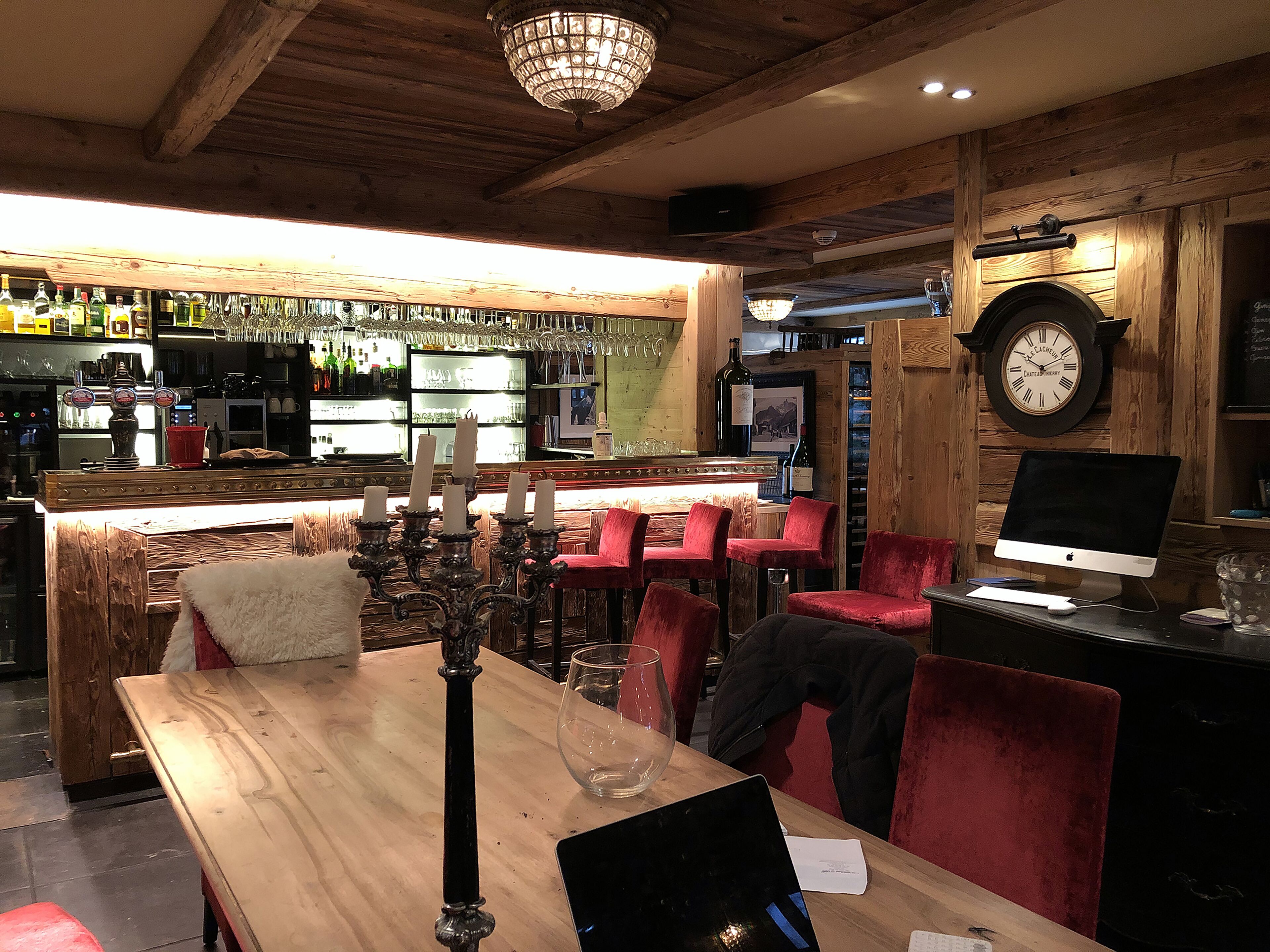 Una zona de bar con mobiliario de madera, una araña y un reloj en la pared.