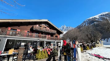 Uma pousada de montanha com área externa, equipamentos de esqui e vista para picos nevados.
