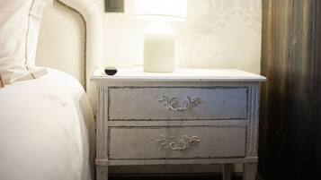 A white bedside table with a lamp, a small drawer, and a wall-mounted switch.