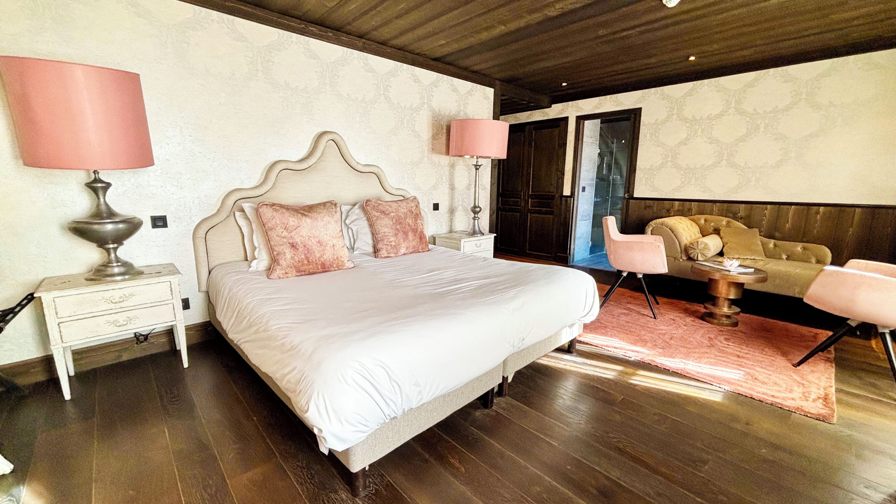 A bedroom with a large bed, bedside lamps, a sofa, and a wooden floor.