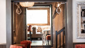 A wooden interior with a dog standing at the entrance, a cozy seating area, and a window with a view. - Chalet Hotel le Castel (Chamonix-Mont-Blanc)