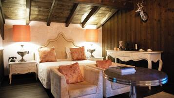Un dormitorio acogedor con techo de madera, una cama con dos almohadas, una mesita de noche con lámpara, una pequeña mesa con libros y un ciervo colgado en la pared.