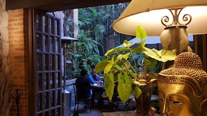 An outdoor dining area with brick walls, a large window, and a Buddha statue. - Casa Aurea (Morelia)