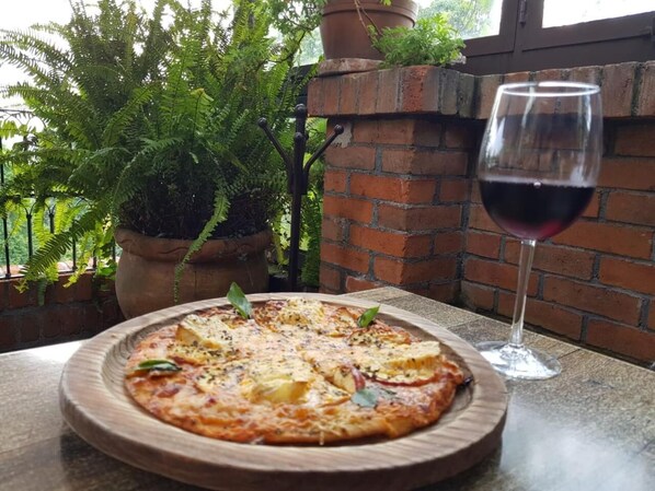 A pizza on a wooden plate with a glass of red wine on a table. - Casa Aurea (Morelia)