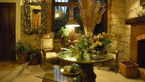 A cozy room with a stone wall, a round table with a vase of flowers, a mirror, and a fireplace. - Casa Aurea (Morelia)