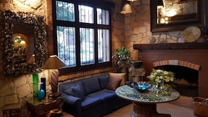 A cozy room with a stone wall, a fireplace, a sofa, and a round table with a decorative bowl. - Casa Aurea (Morelia)