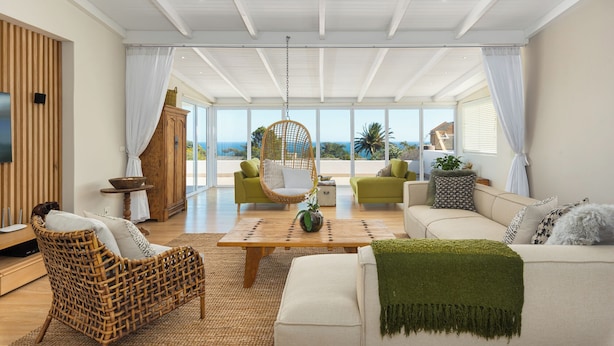 Un salón espacioso con techo alto, ventanas grandes y vista al océano.