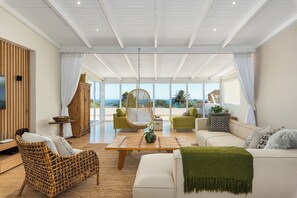 Ein großzügiges Wohnzimmer mit hoher Decke, großen Fenstern und Meerblick.