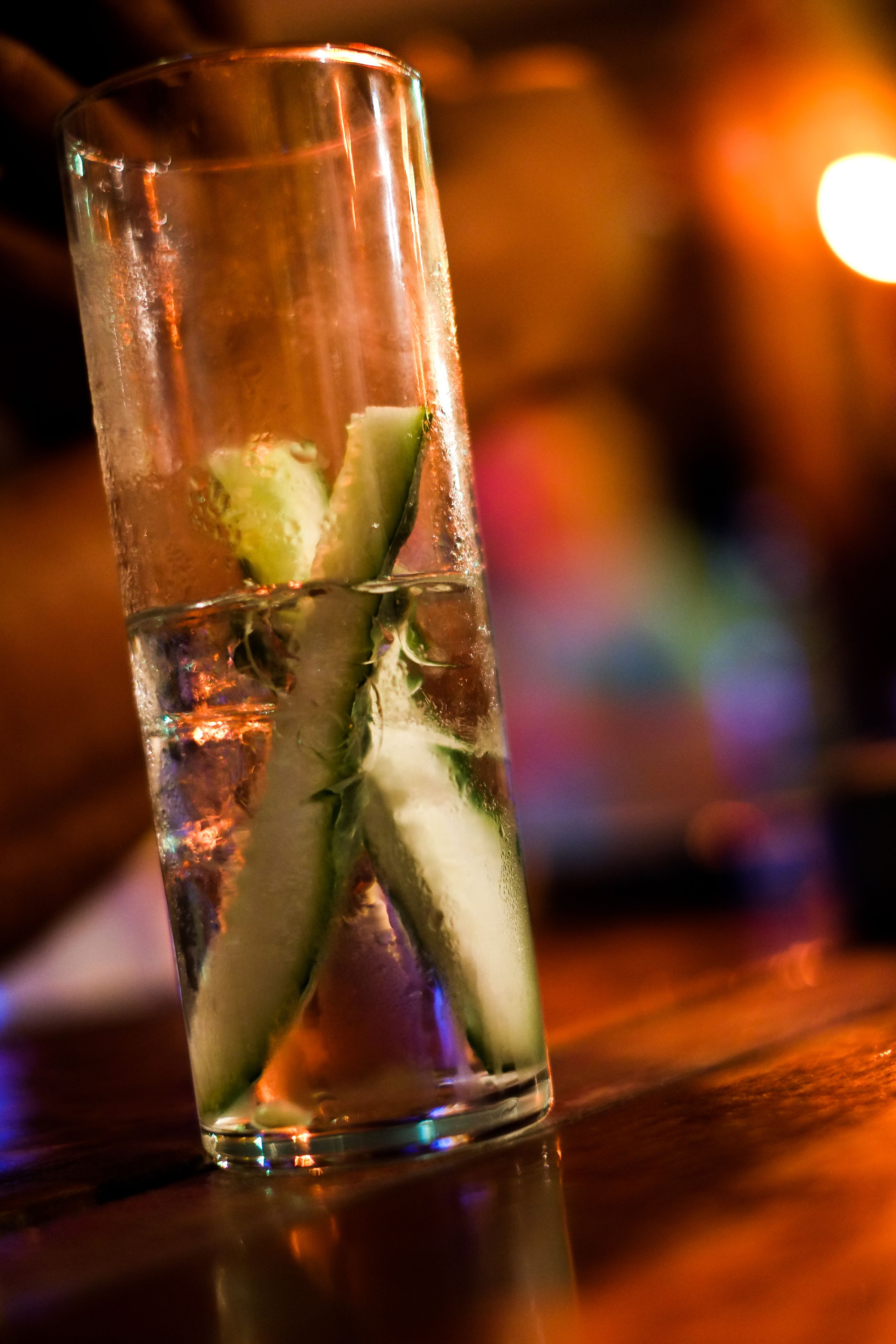 A clear glass with ice cubes and a slice of lime, reflecting on a wooden surface.