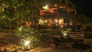Un bâtiment à deux étages comprenant un bar, entouré d’une végétation tropicale et dot é d’une terrasse en bois avec des chaises longues.