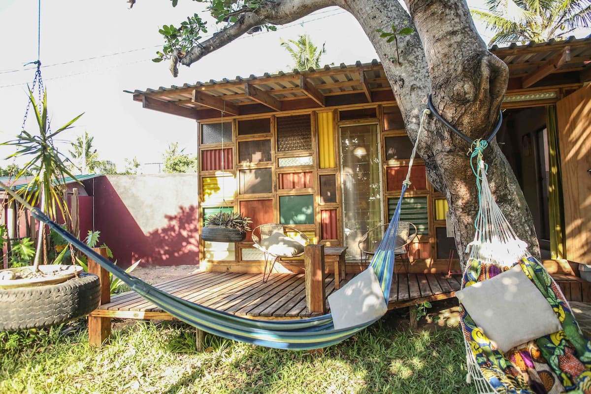 A wooden house with a porch, a hammock, and a tire planter.