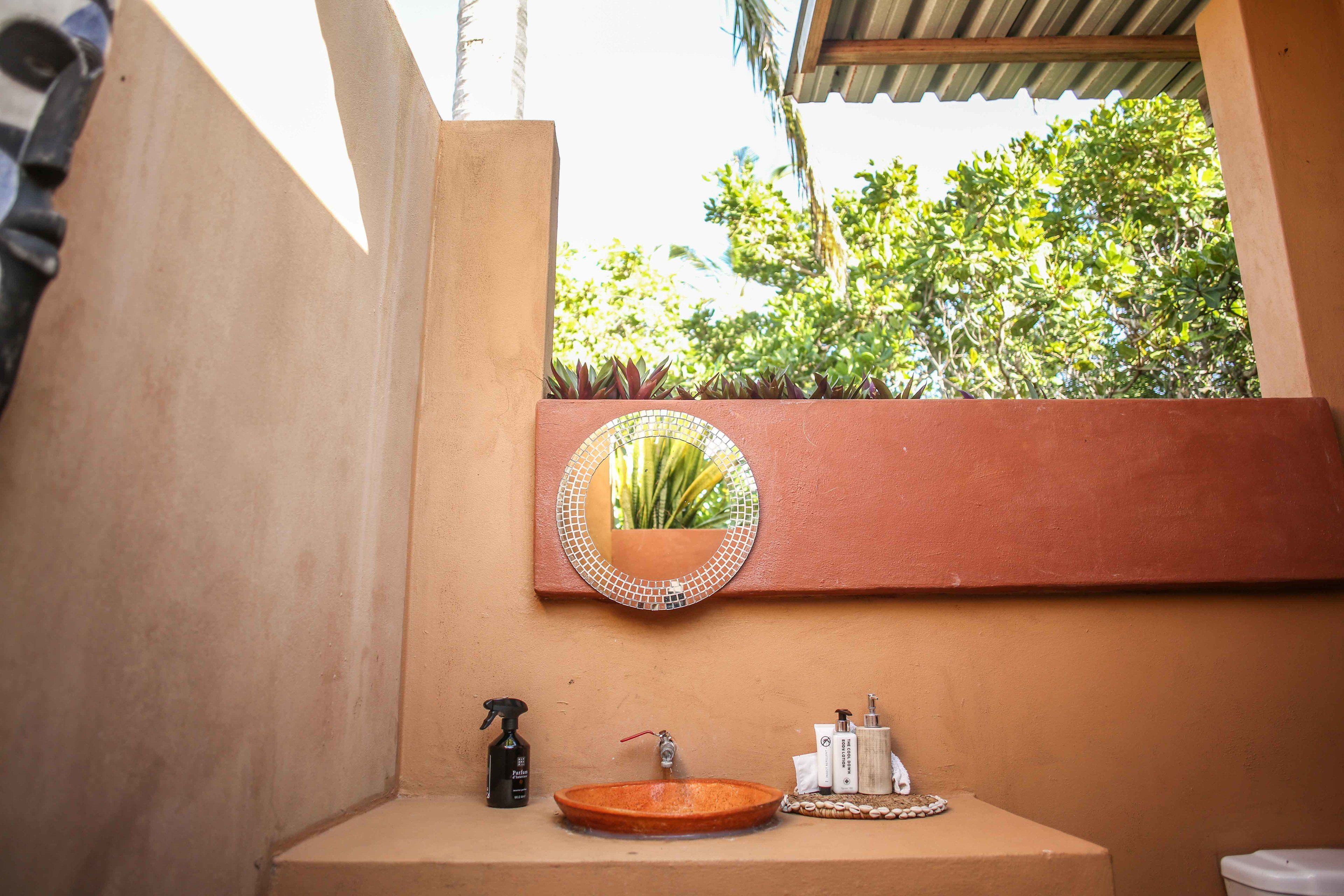 A bathroom with a round mirror, a sink, and toiletries.