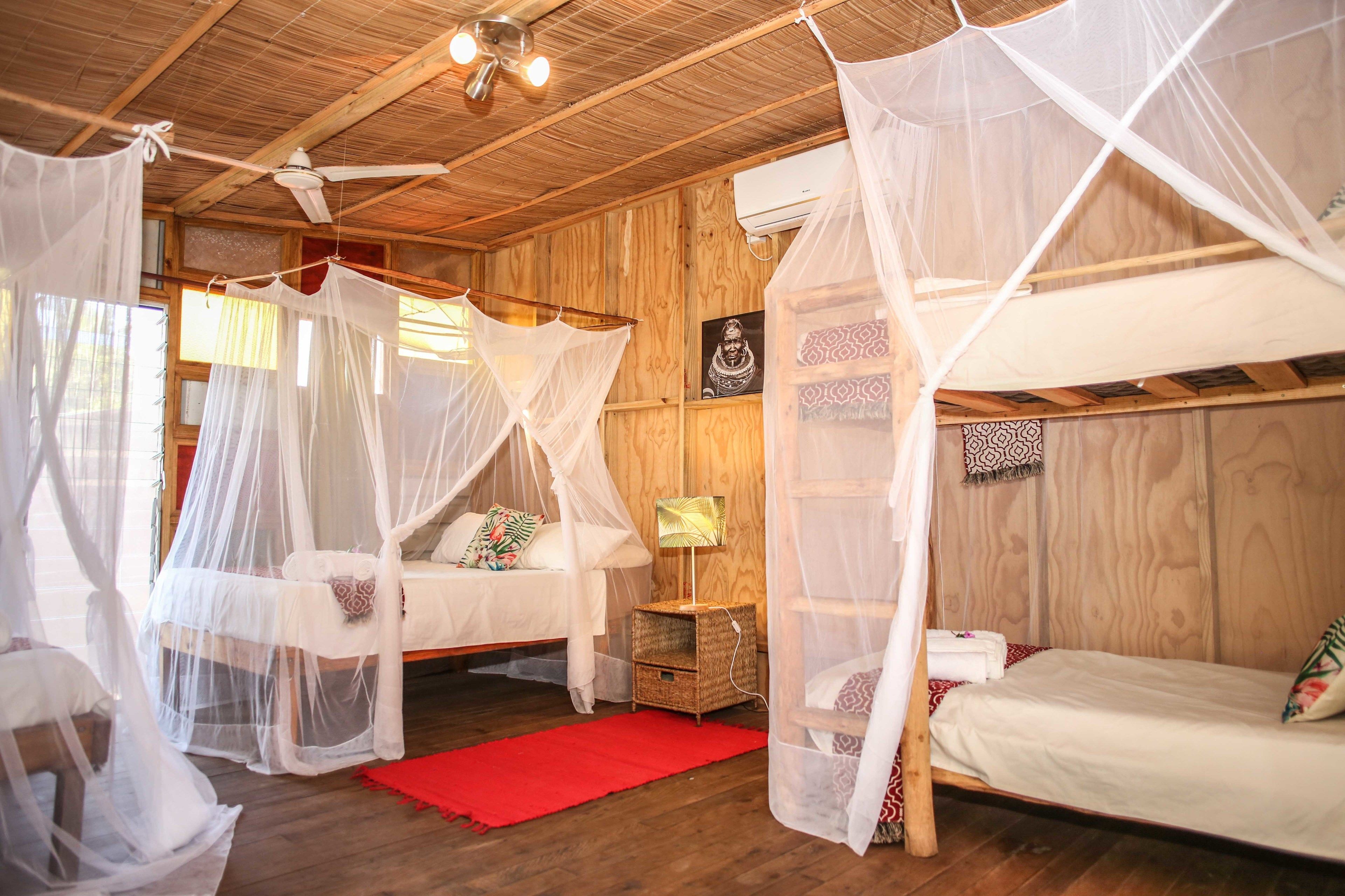 Una habitación con dos camas, cada una con dosel, paredes de madera, una alfombra roja y un ventilador de techo.