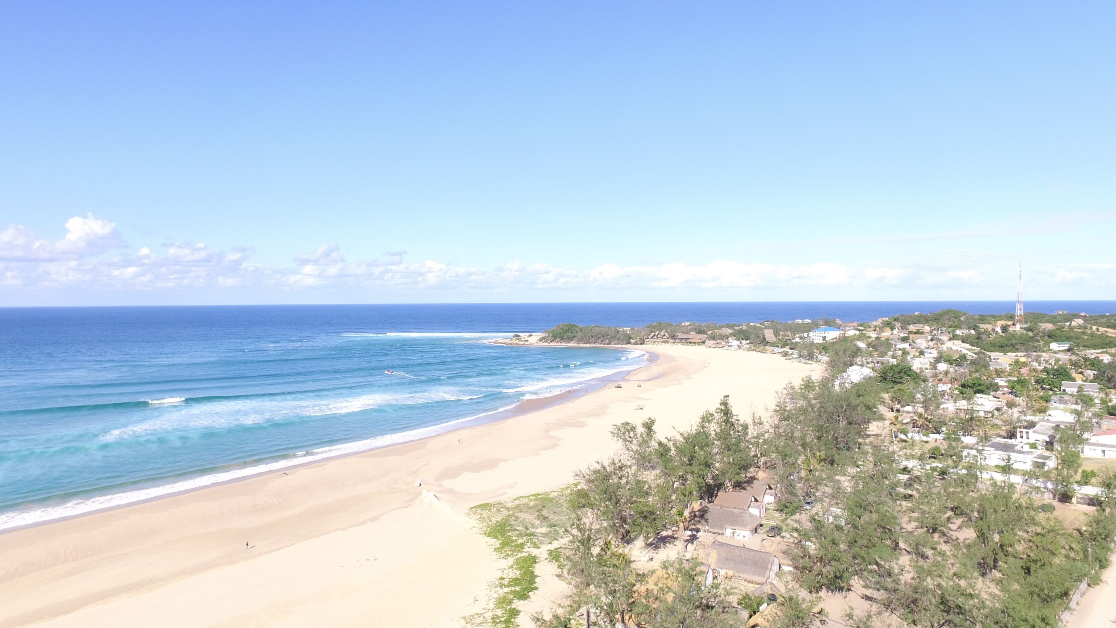 Un pueblo costero con una playa arenosa, aguas azules cristalinas y una combinación de edificios residenciales y comerciales.