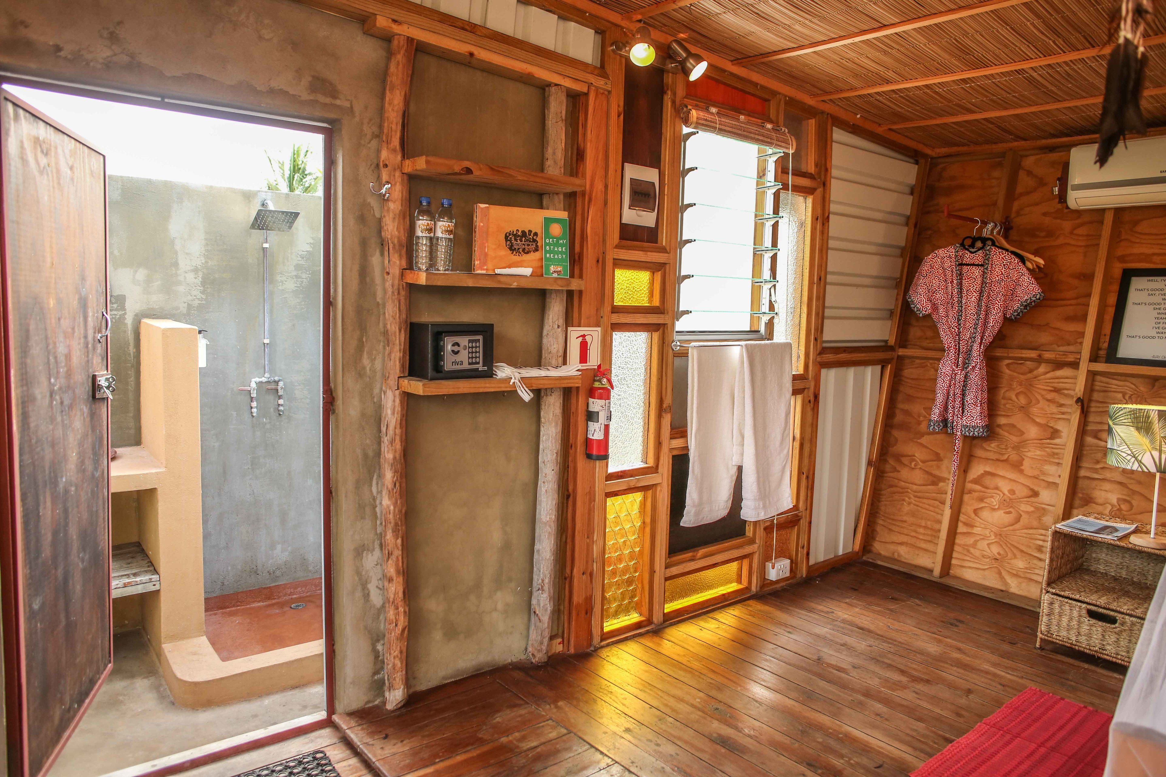 A wooden interior with a shower, shelves with toiletries, a fire extinguisher, and a hanging robe.