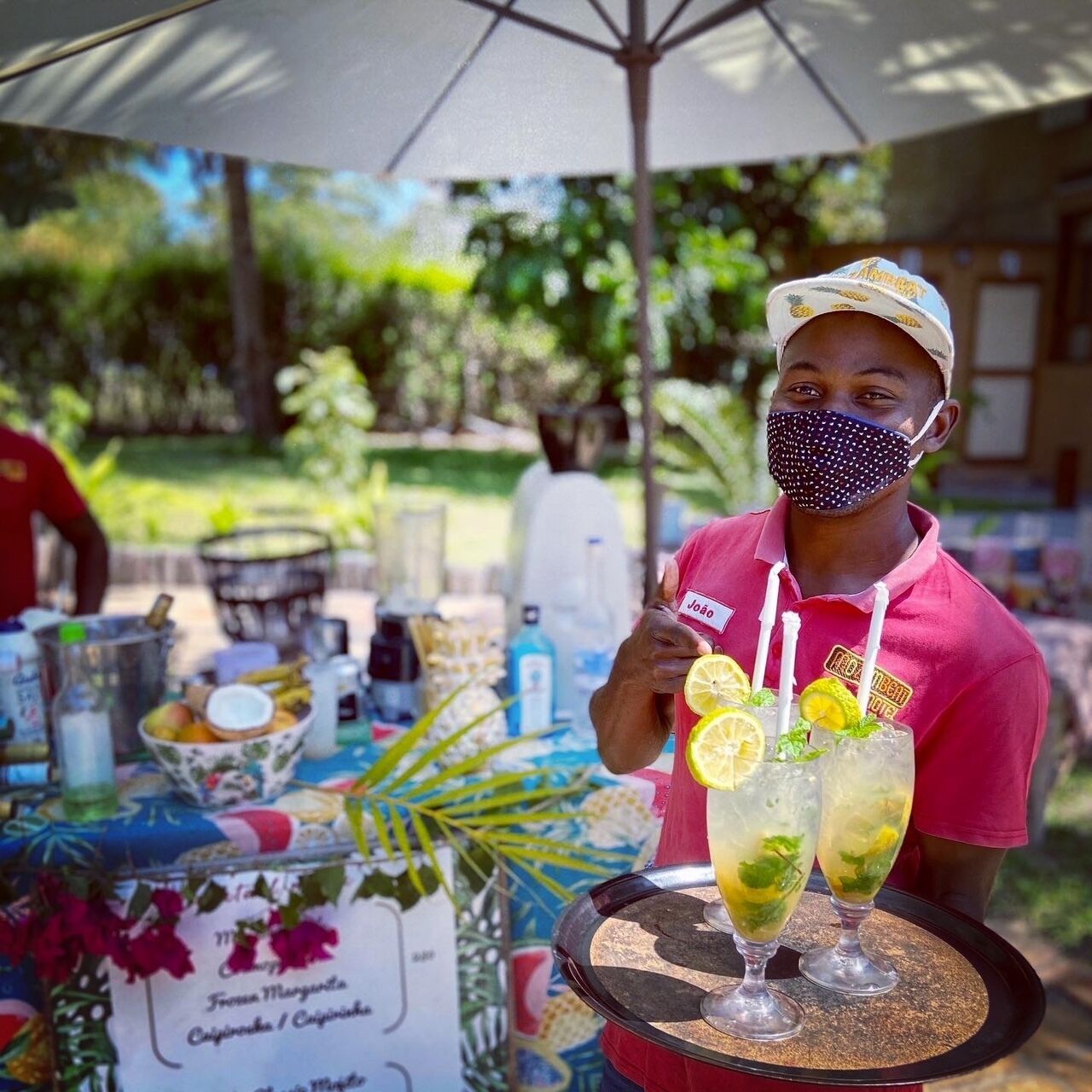 A person serving drinks at an outdoor event with a table displaying various items and a menu.