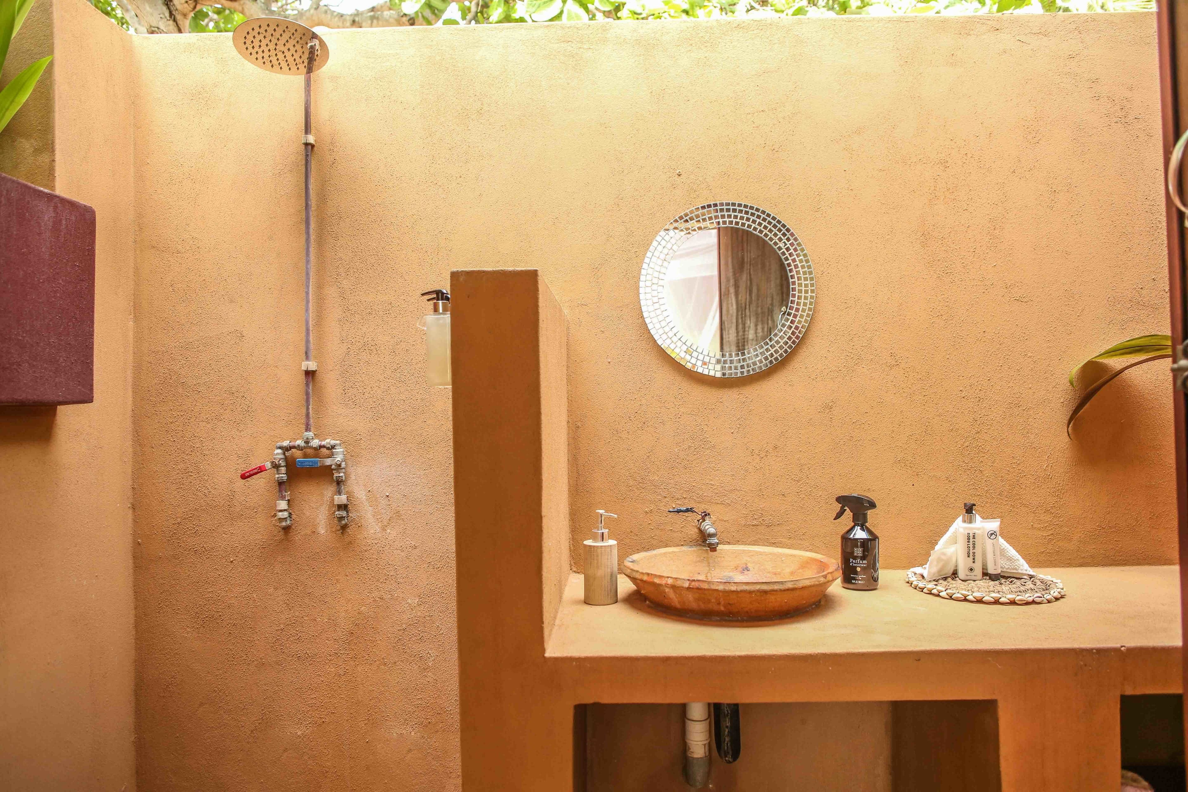 A bathroom with a wooden sink, a round mirror, a handheld showerhead, and a bottle of shampoo.