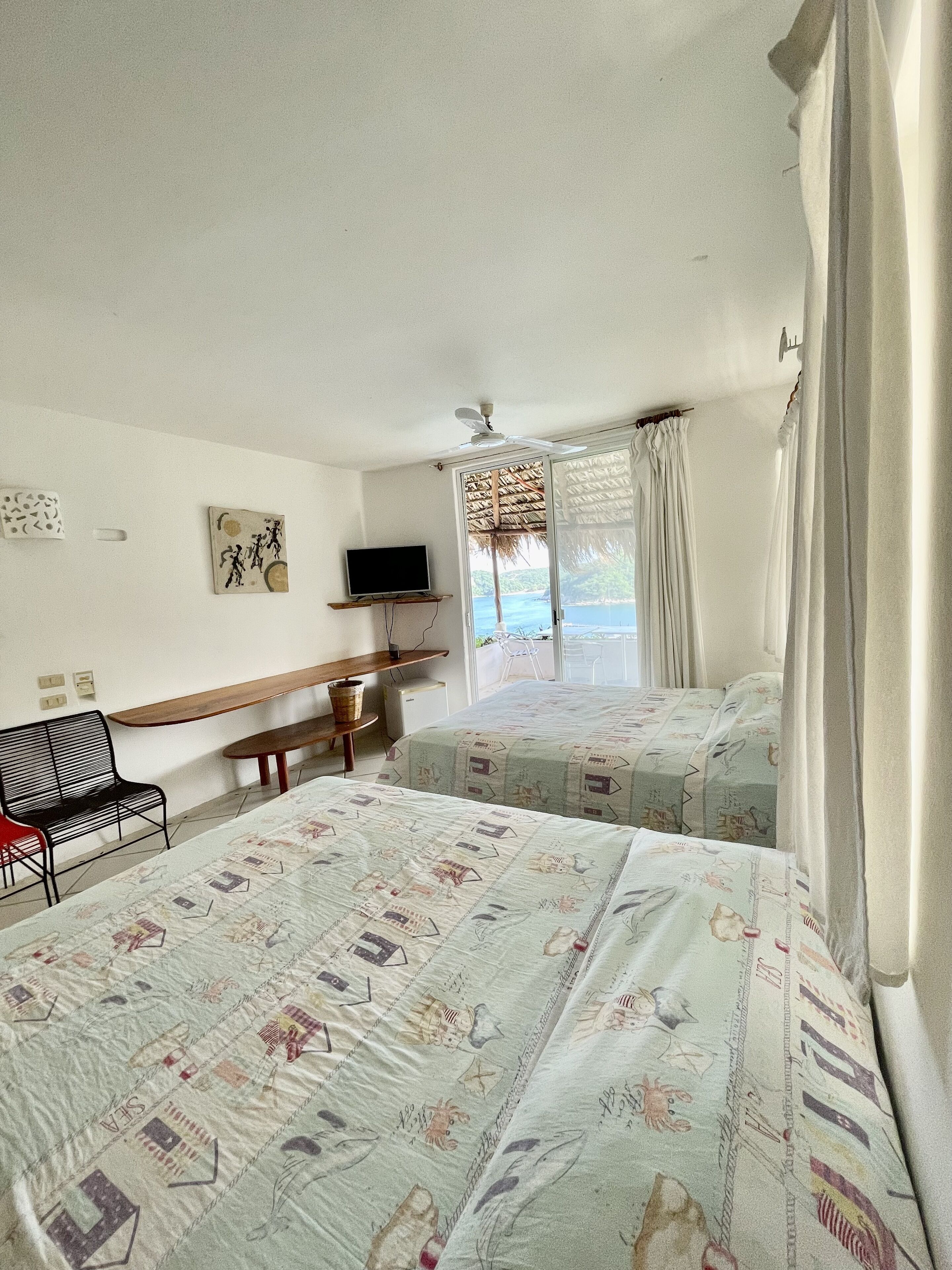 Habitación de hotel con dos camas, un escritorio, una silla, televisión y vista al mar.