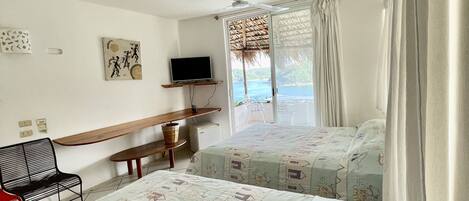 Habitación de hotel con dos camas, un escritorio, una silla, televisión y vista al mar.