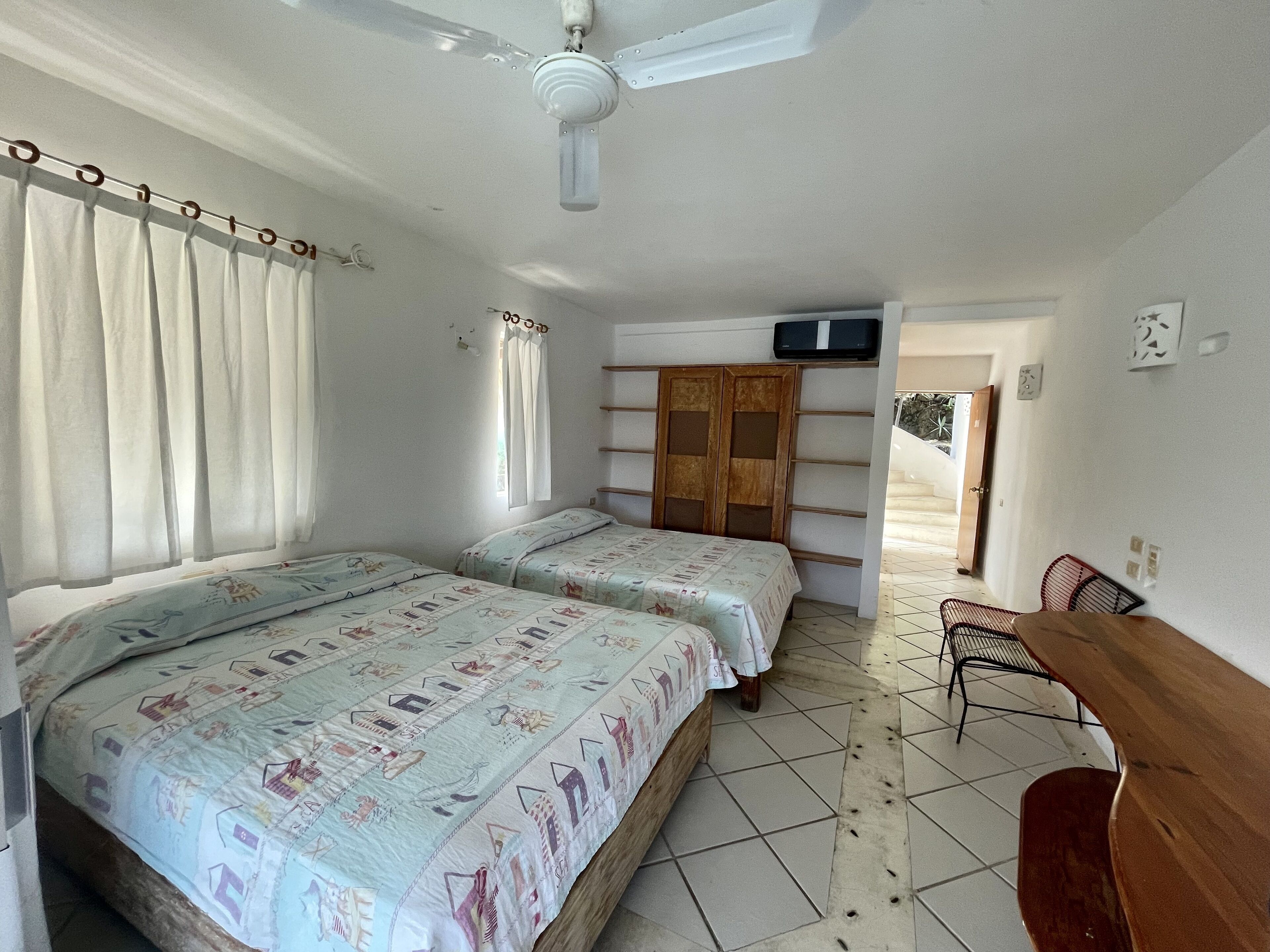 A bedroom with two beds, a ceiling fan, a TV, and a wooden desk.