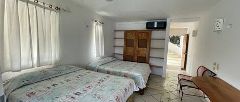 A bedroom with two beds, a ceiling fan, a TV, and a wooden desk.