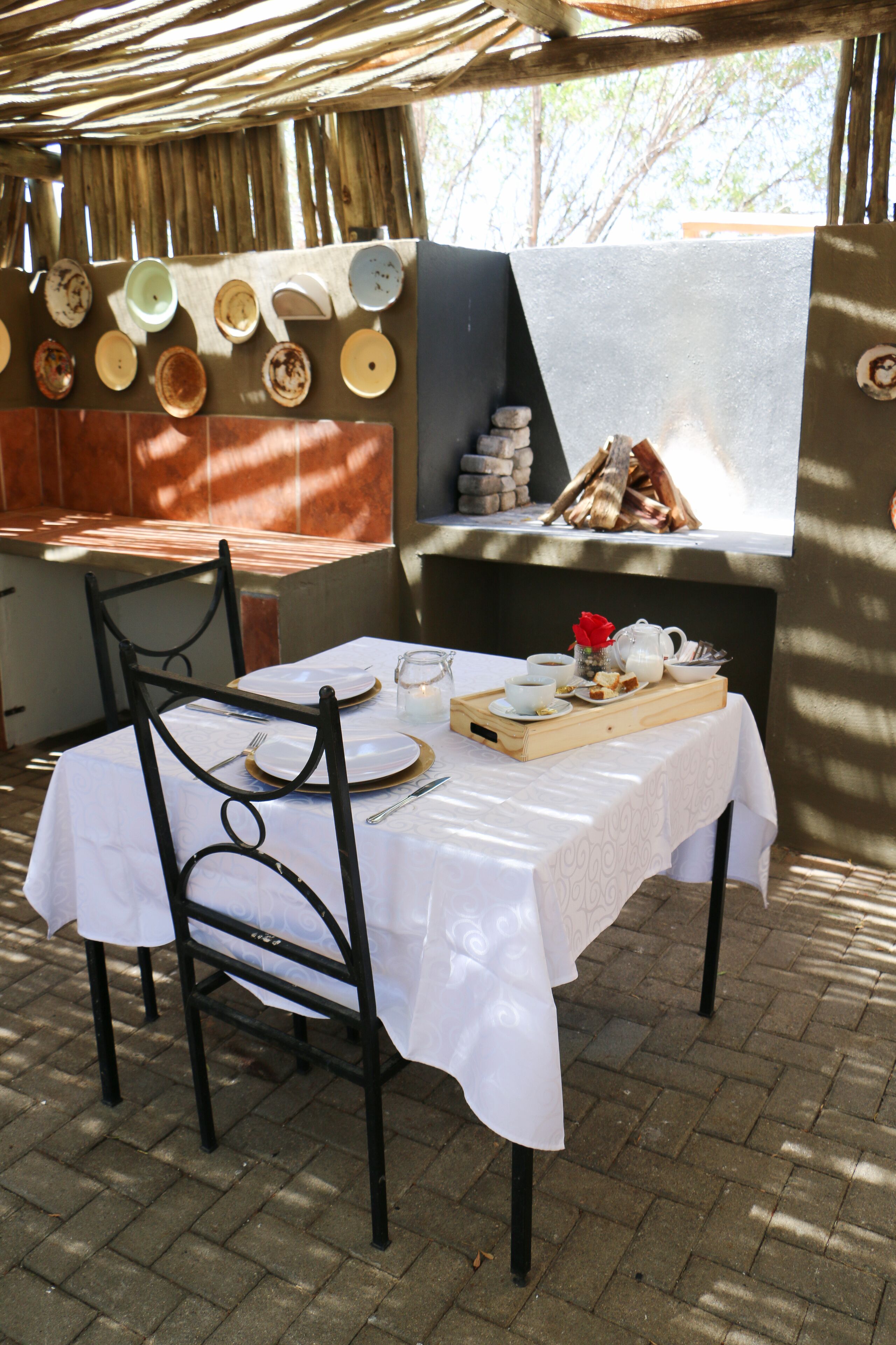 Un espacio exterior para comer con una mesa dispuesta para dos, una parrilla y una pared decorada con platos.