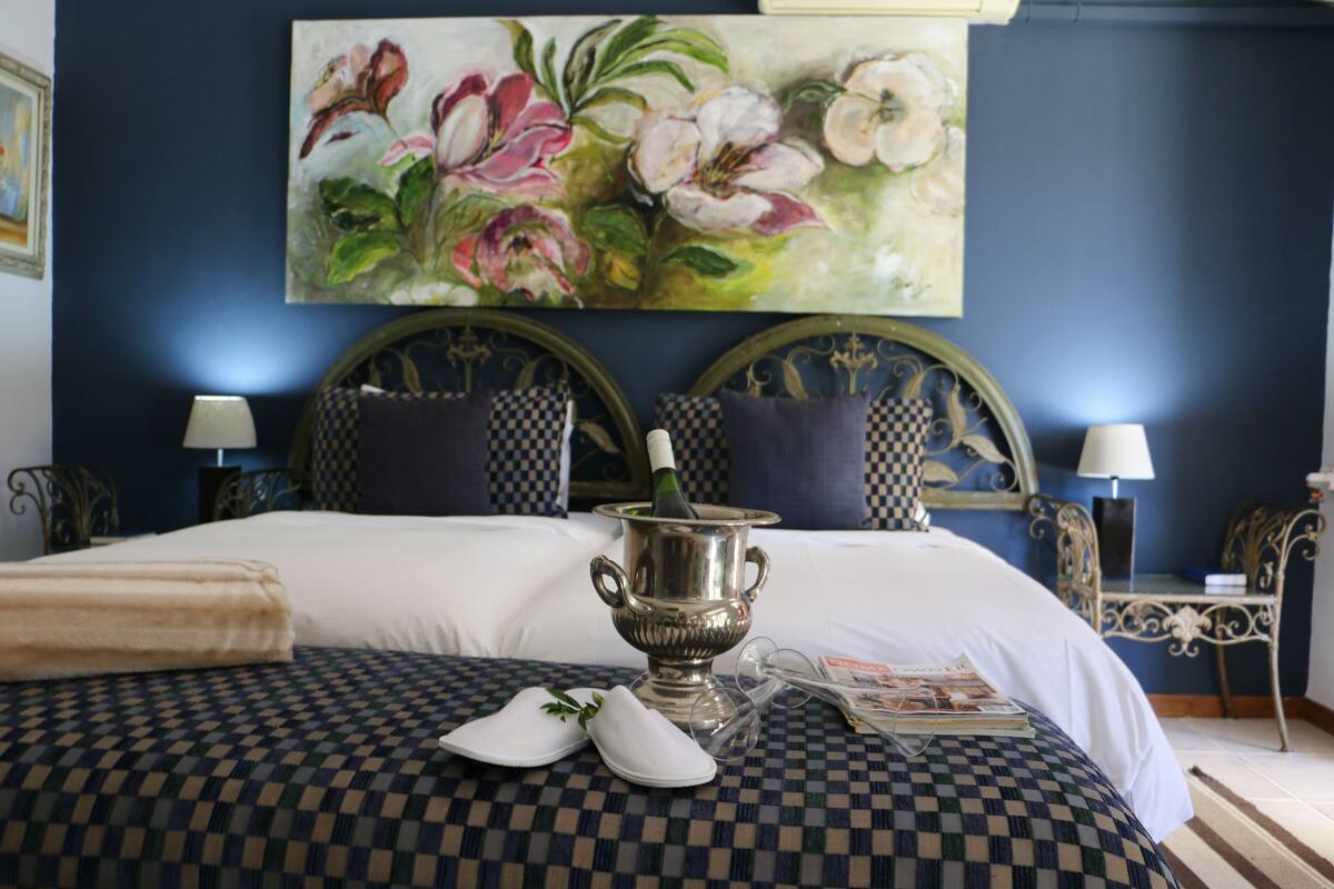 A neatly made bed with checkered bedding, a silver vase, and slippers on a checkered pillow.
