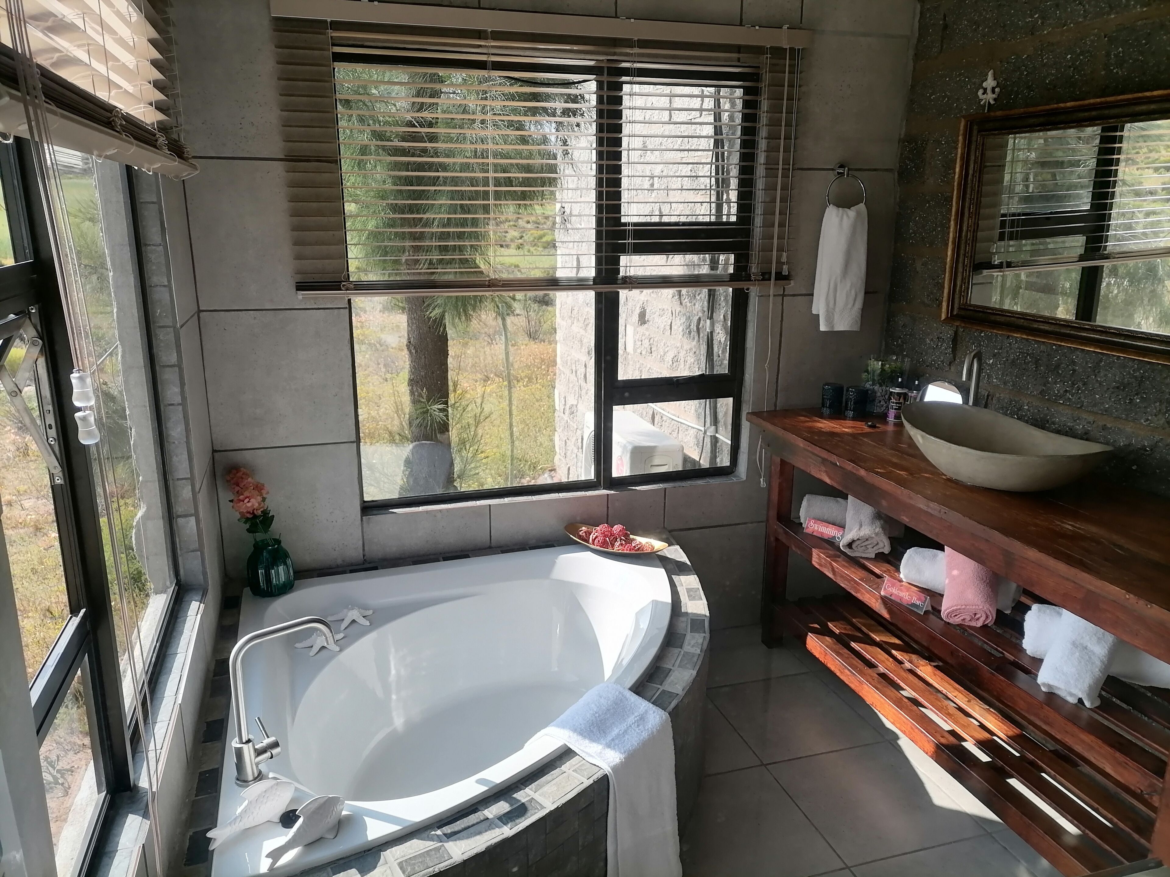 Ein Badezimmer mit einer großen Badewanne, einem hölzernen Waschtisch mit Waschbecken und einem Fenster mit Jalousien.