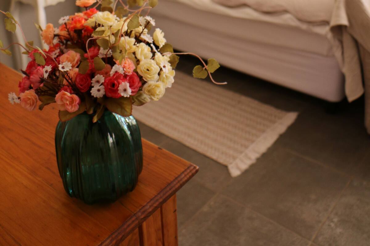A bedroom with a bed, bedside table, lamp, and a vase with flowers.