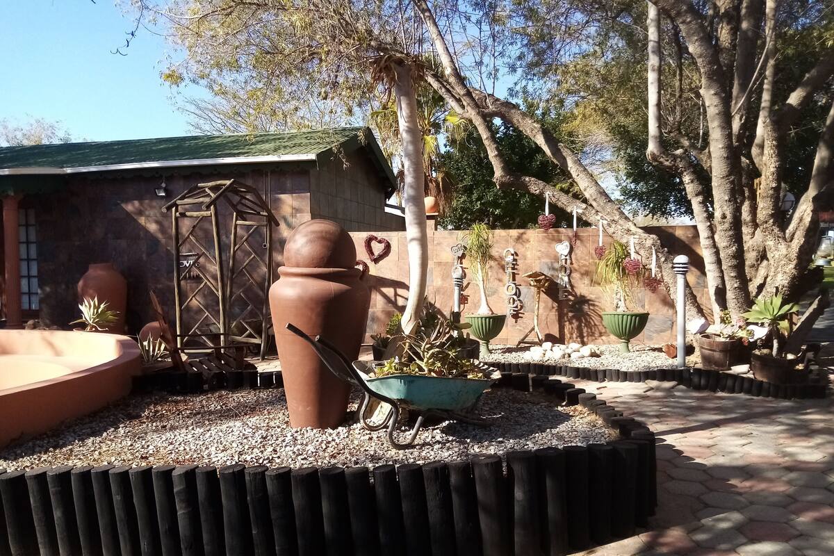 A garden area with a large terracotta pot, a wheelbarrow, and various potted plants.