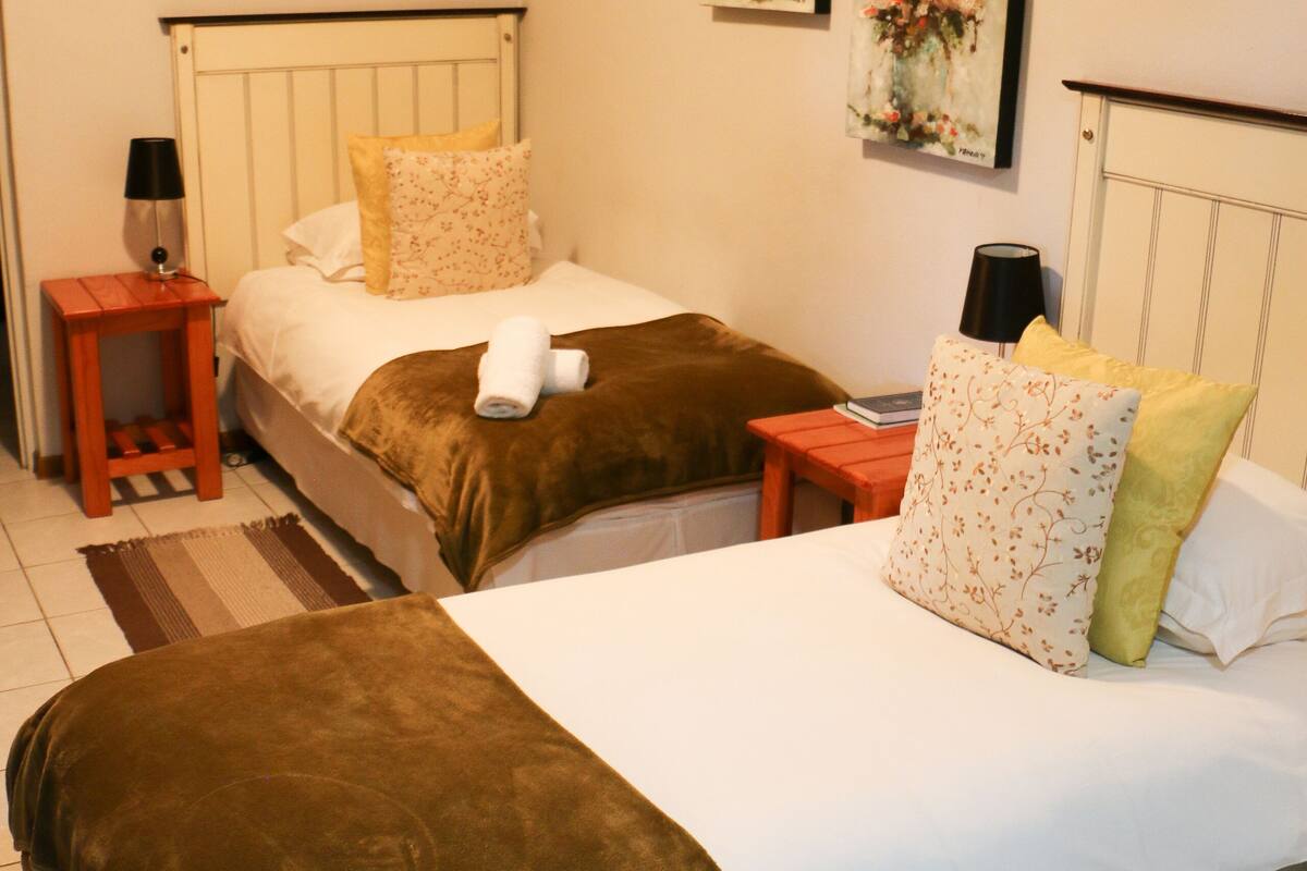 A hotel room with two beds, a nightstand, a lamp, and a radiator.